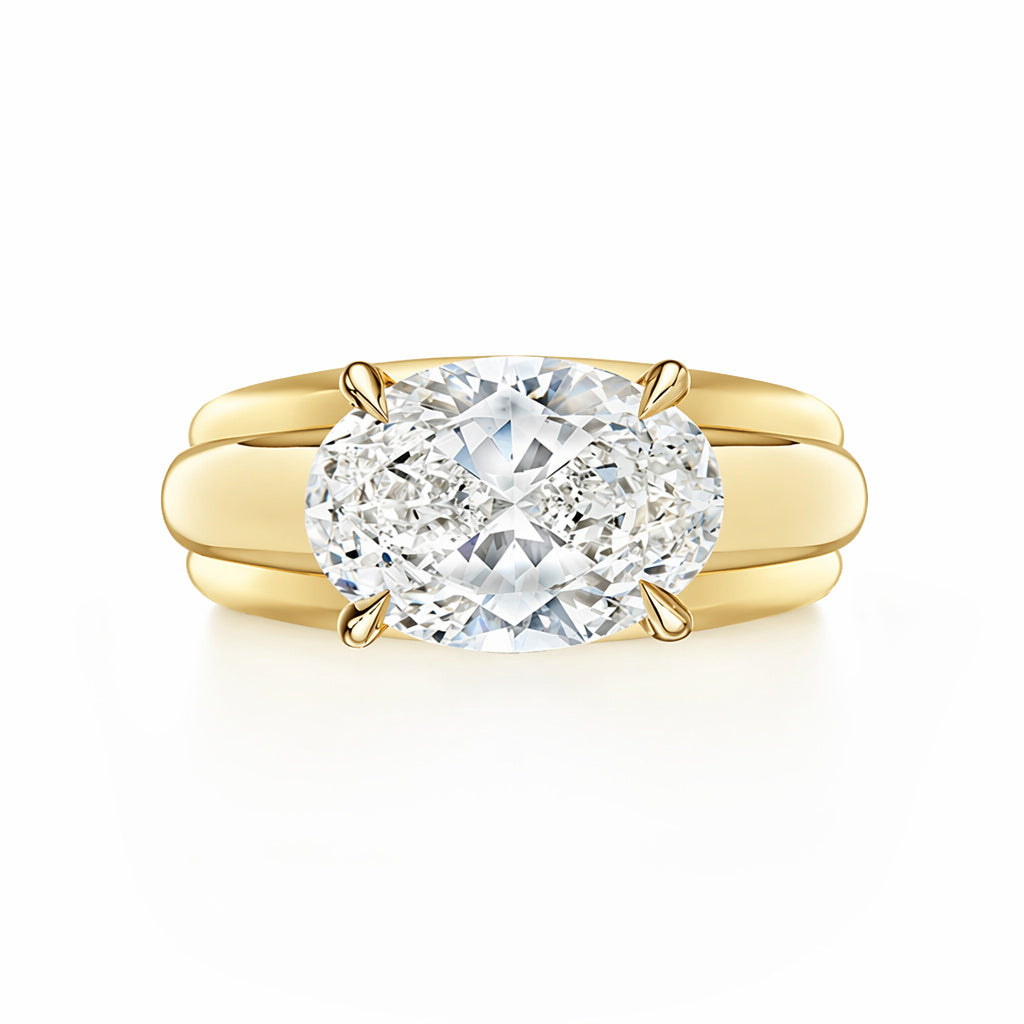 The East-West Set Oval Diamond Ribbed Engagement Ring in yellow gold features a wide band and large oval diamond in a four-prong setting, shown against a white background.