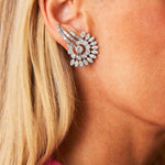 Close-up of a woman’s ear adorned with Cartier Diamond Earclips, circa 1950s—large, intricate earrings in a sunburst design reminiscent of platinum Cartier Paris styles; she has blonde hair and wears a pink-collared garment.