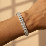 A close-up of a wrist wearing the Cartier Mid-Century Diamond Bracelet, with sparkling square and rectangular links, captured in natural light on a beige background.