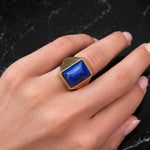 A hand with neatly manicured nails wears the Boucheron Lapis Lazuli and Gold Ring, circa 1930—crafted from 18 karat gold and featuring a striking lapis pyramid gemstone in a geometric design—set against a black marble background.