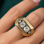 A hand with light pink nail polish wears the Mauboussin Gold and Diamond Ring, circa 1940, which features three large round diamonds surrounded by four smaller diamonds in a geometric rectangular design crafted from 18K white gold.