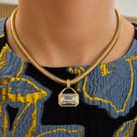 A close-up of a person wearing the East-West Bezel Set Emerald Cut Diamond Pendant Necklace in Yellow Gold over a textured black, blue, and yellow patterned top.