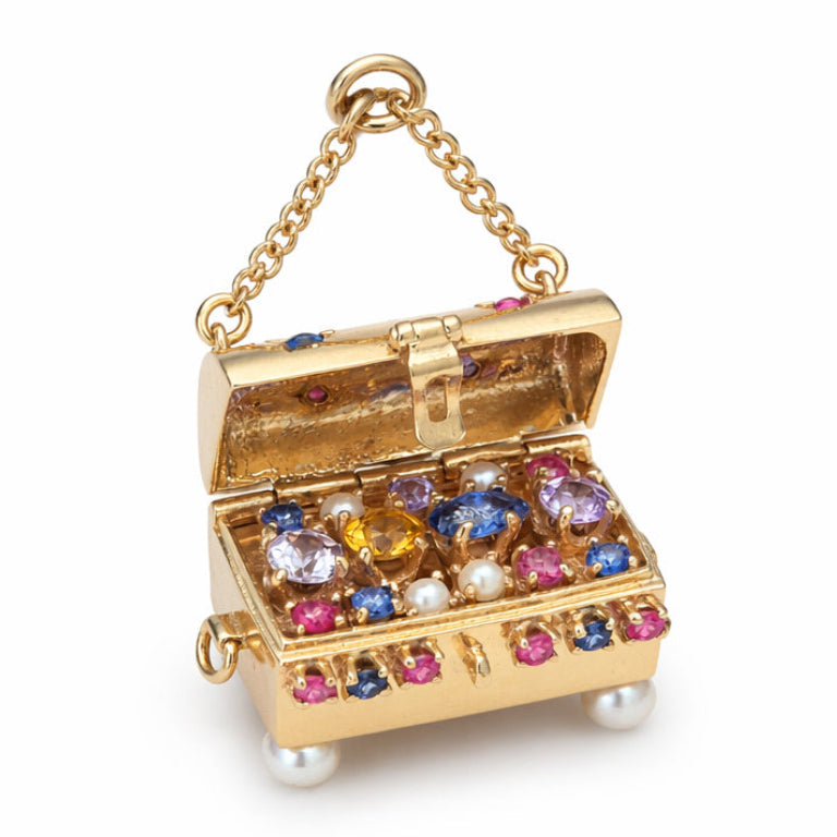 The Gold and Gem-Set Charm is a small 14K gold treasure chest, adorned with colorful gemstones, rubies, and pearls. It features a chain handle and overflows with sparkling jewels and pearls inside.