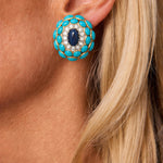 Close-up of a woman's ear adorned with a Van Cleef & Arpels pair of Sapphire, Turquoise and Diamond Earclips, featuring large round earrings set with turquoise stones around the edge, a central dark blue sapphire cabochon, and small white diamonds; her blonde hair is partially visible.