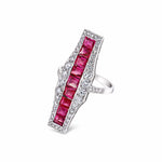 The Ruby and Diamond Ring is crafted in white gold and showcases a long rectangular setting with vibrant square-cut rubies at its center, elegantly bordered by small round European-cut diamonds. It is displayed against a white background.