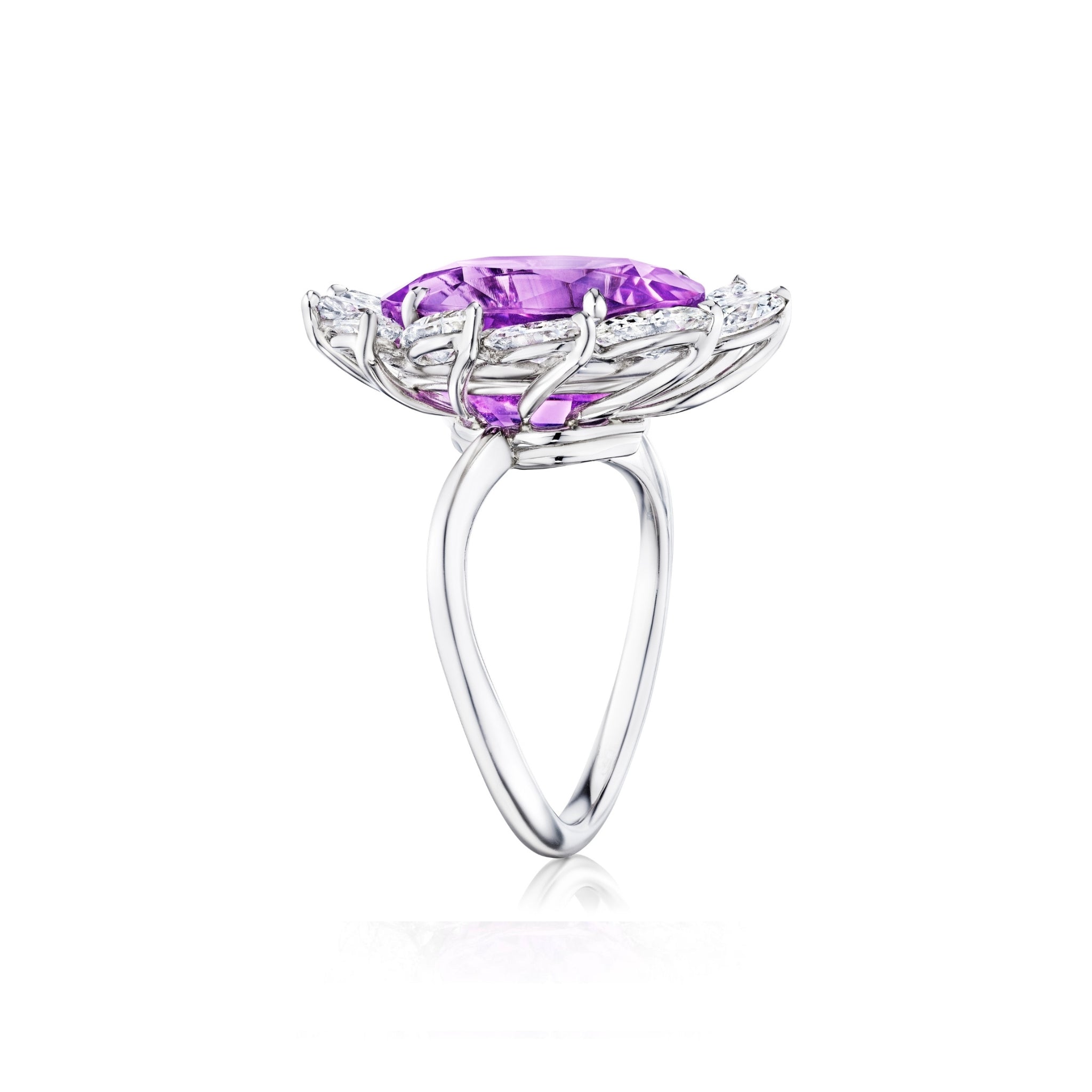 A side view of the Sunburst Cocktail Ring showcases its 18k white gold band, featuring a large oval purple sapphire centerpiece set in an intricate floral-inspired design and accented with a halo of small marquise diamonds, displayed against a white background.