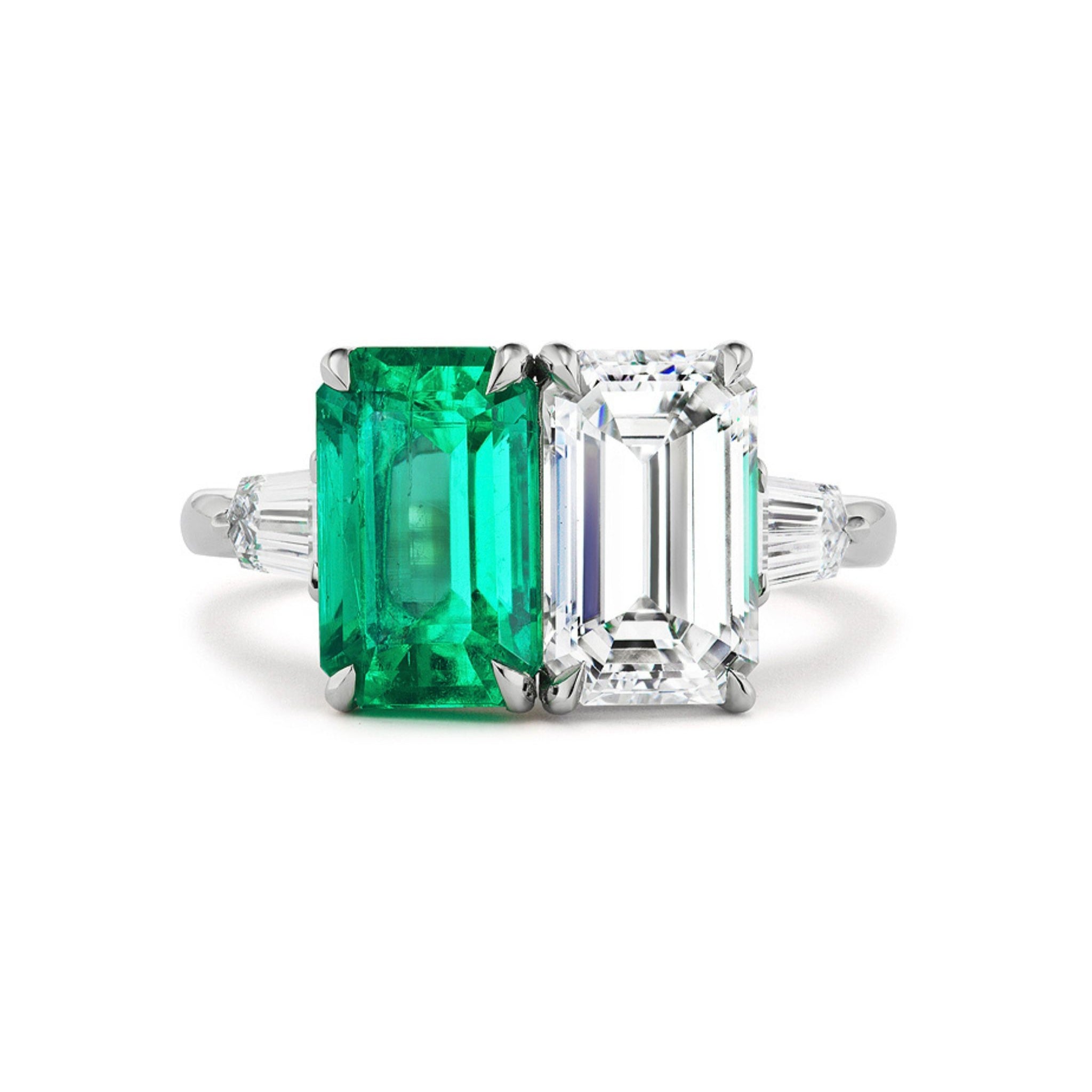 Celebrate with the elegant Toi et Moi Ring, showcasing a rectangular emerald-cut diamond and a vibrant green emerald set side by side, each accented by tapered baguette diamonds on a sleek silver band.