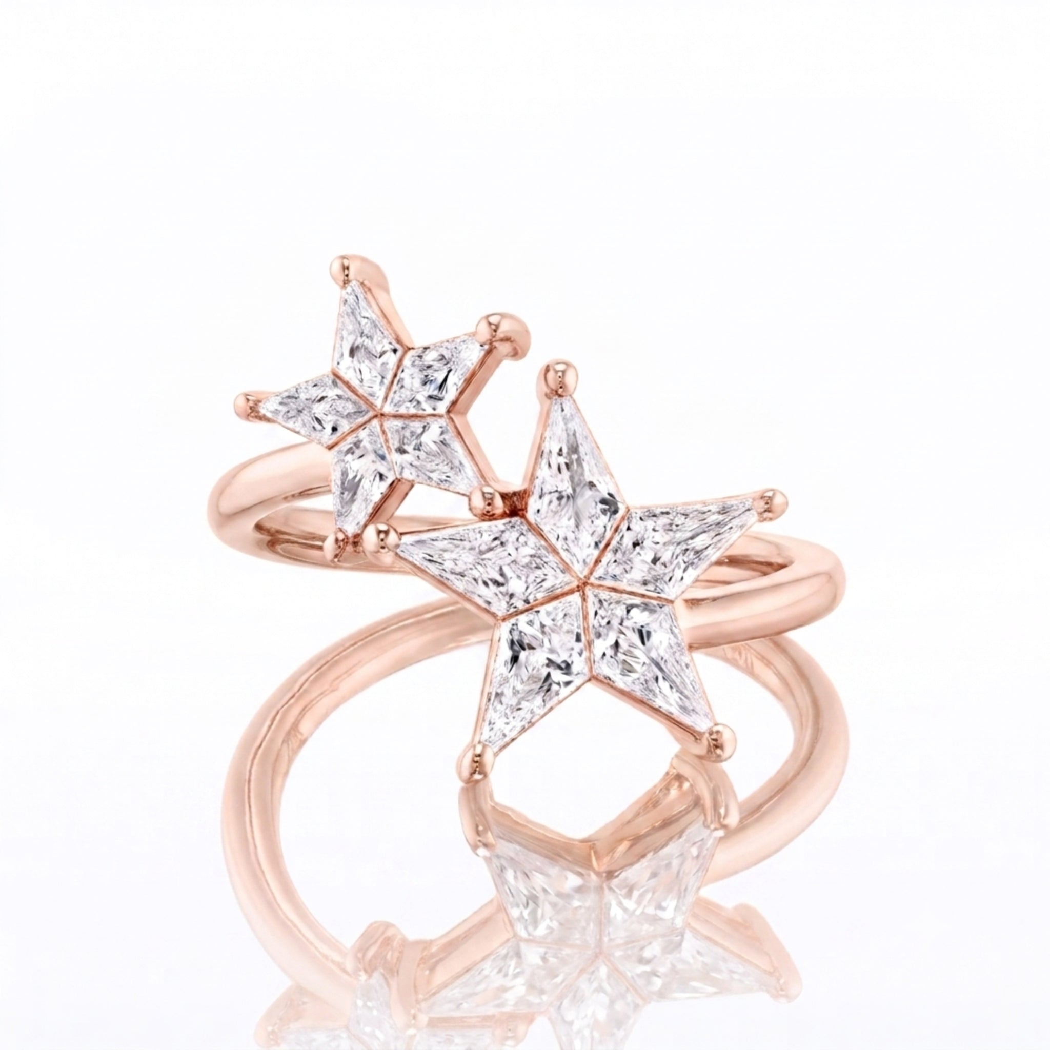 The Celestial Shooting Stars Wraparound Ring with Kite Diamonds from the Celestial Collection is a stunning 18k gold ring, featuring two overlapping star-shaped designs adorned with sparkling kite-shaped diamonds, beautifully displayed on a reflective white surface.