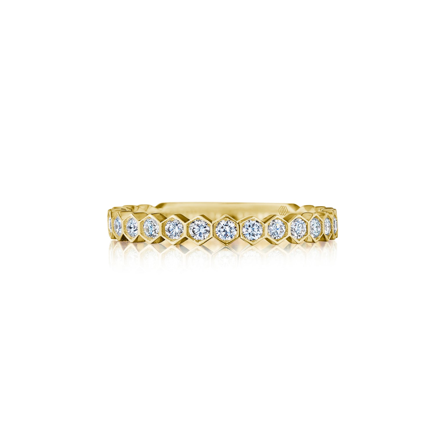 The Hexagon Bezel Set Diamond Band in 18k gold showcases a continuous row of round white diamonds, each set in hexagonal bezels, displayed against a white background.