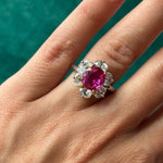 A hand wearing the Vintage Oscar Heyman & Brothers Pink Sapphire and Diamond Ring, showcasing a large Ceylon pink sapphire center gemstone encircled by sparkling diamonds, set against a green background.