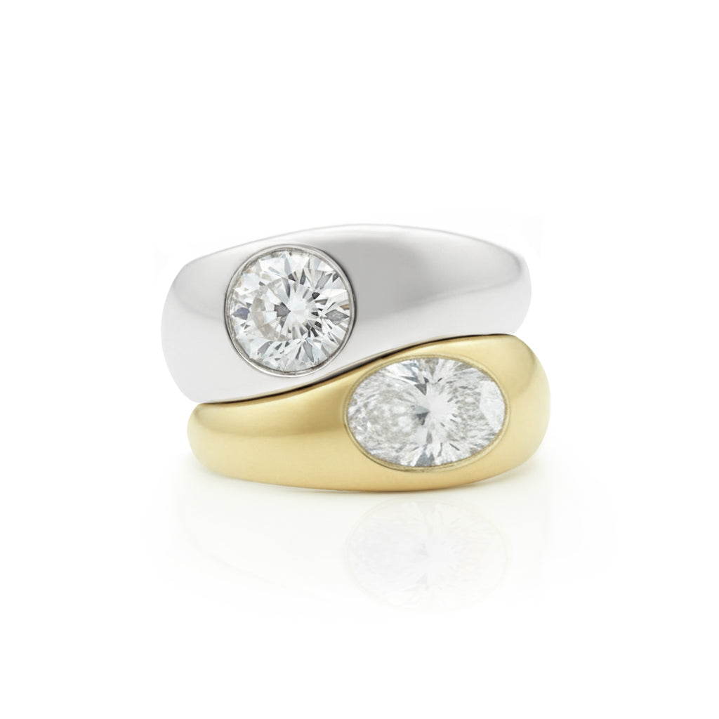 The Stacked Burnish Set Round Diamond in White Gold and Oval Shape Diamond in Yellow Gold Engagement Ring features two rings—one white gold with a round diamond, the other yellow gold with an oval diamond—stacked on a white background.