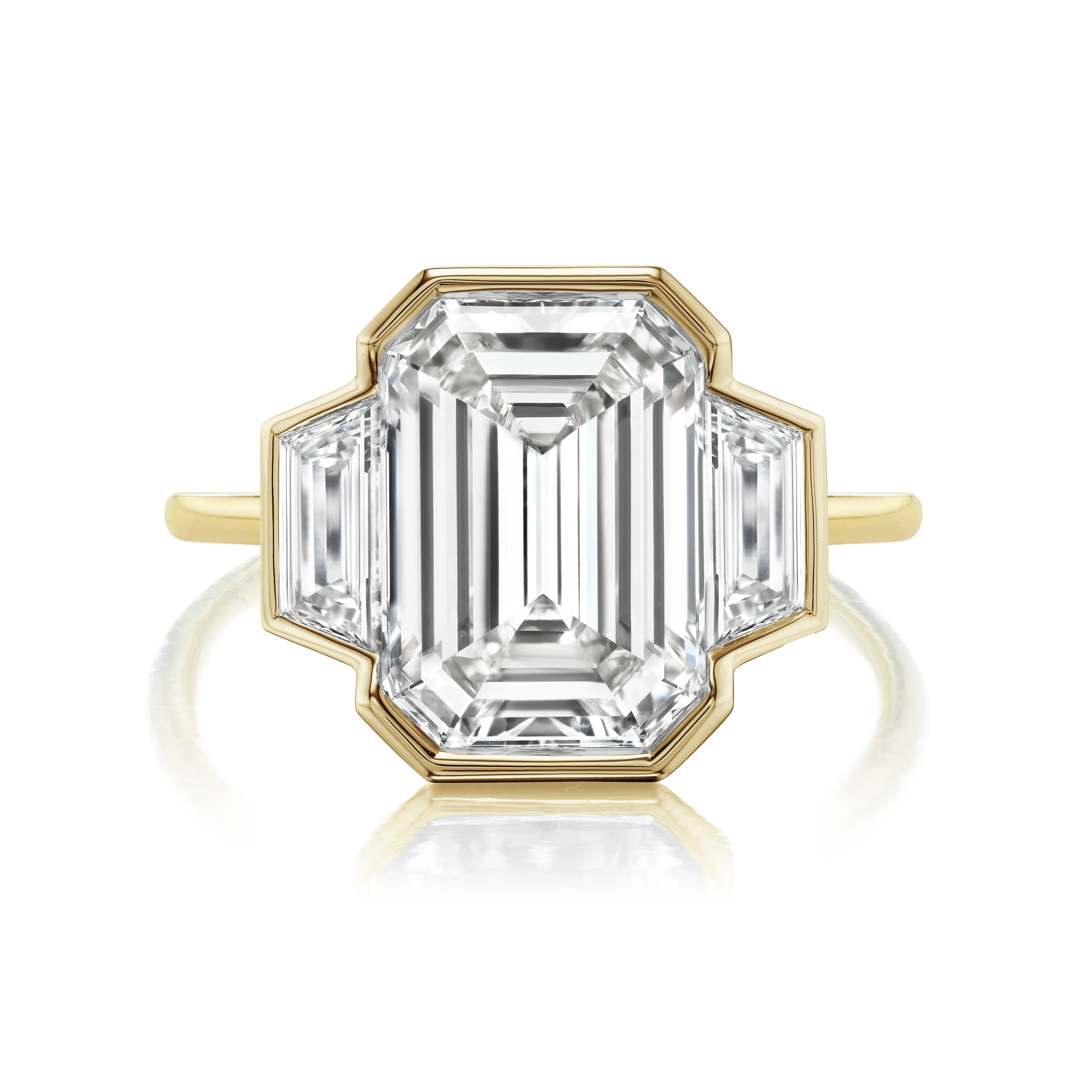 A Half Bezel Set Three Stone Engagement Ring showcases an emerald cut diamond center with trapezoid side stones, set in a modern, angular design.