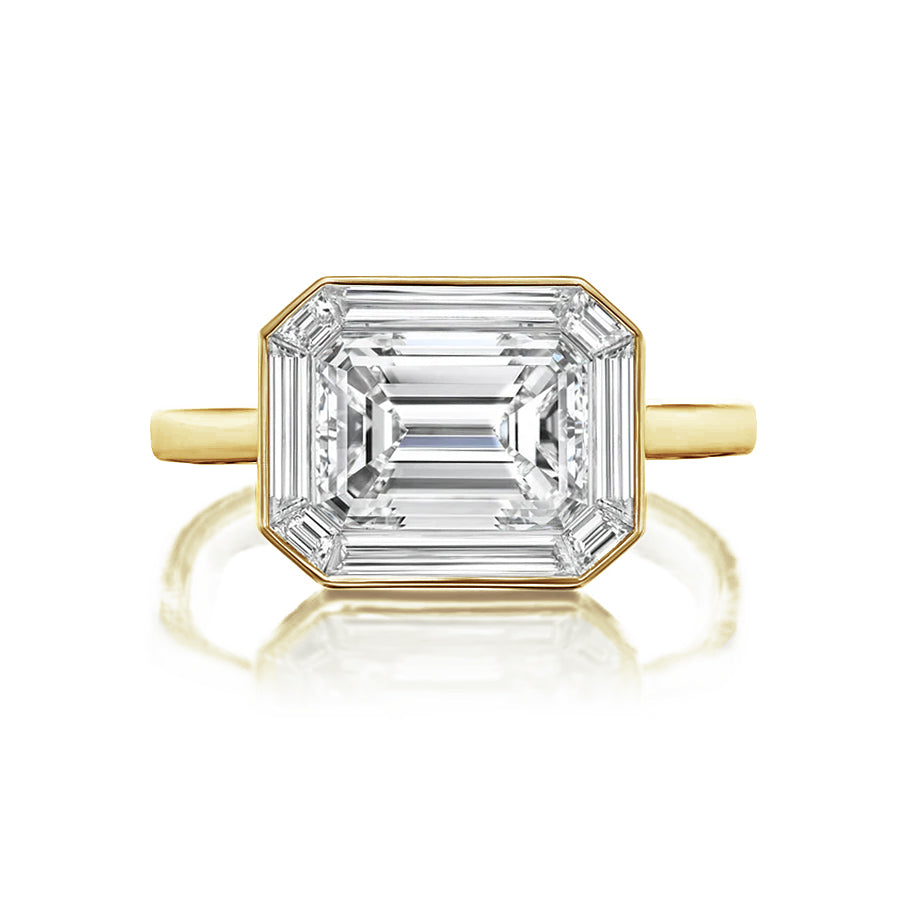 The East-West Set Mosaic Diamond Engagement Ring features an emerald cut diamond with beveled corners, a baguette halo, and a simple white gold band, displayed against a white background.