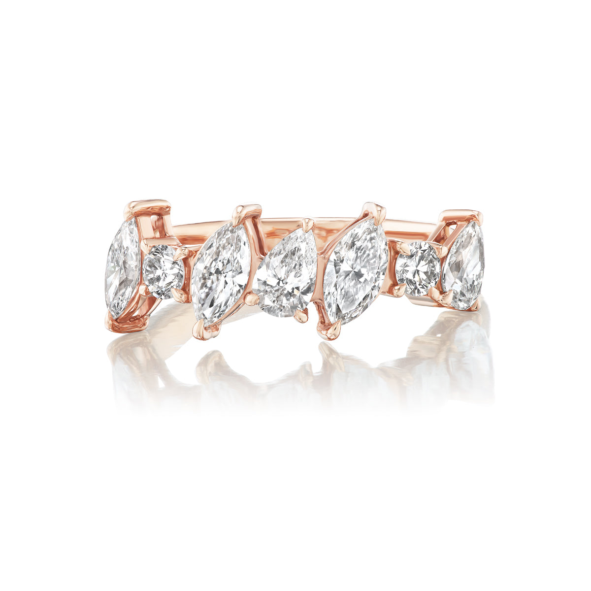 The Diagonally Set Mixed Shape Diamond Half Eternity Band in 18K rose gold features marquise, pear, and round diamonds set in prongs, beautifully displayed on a reflective white surface.