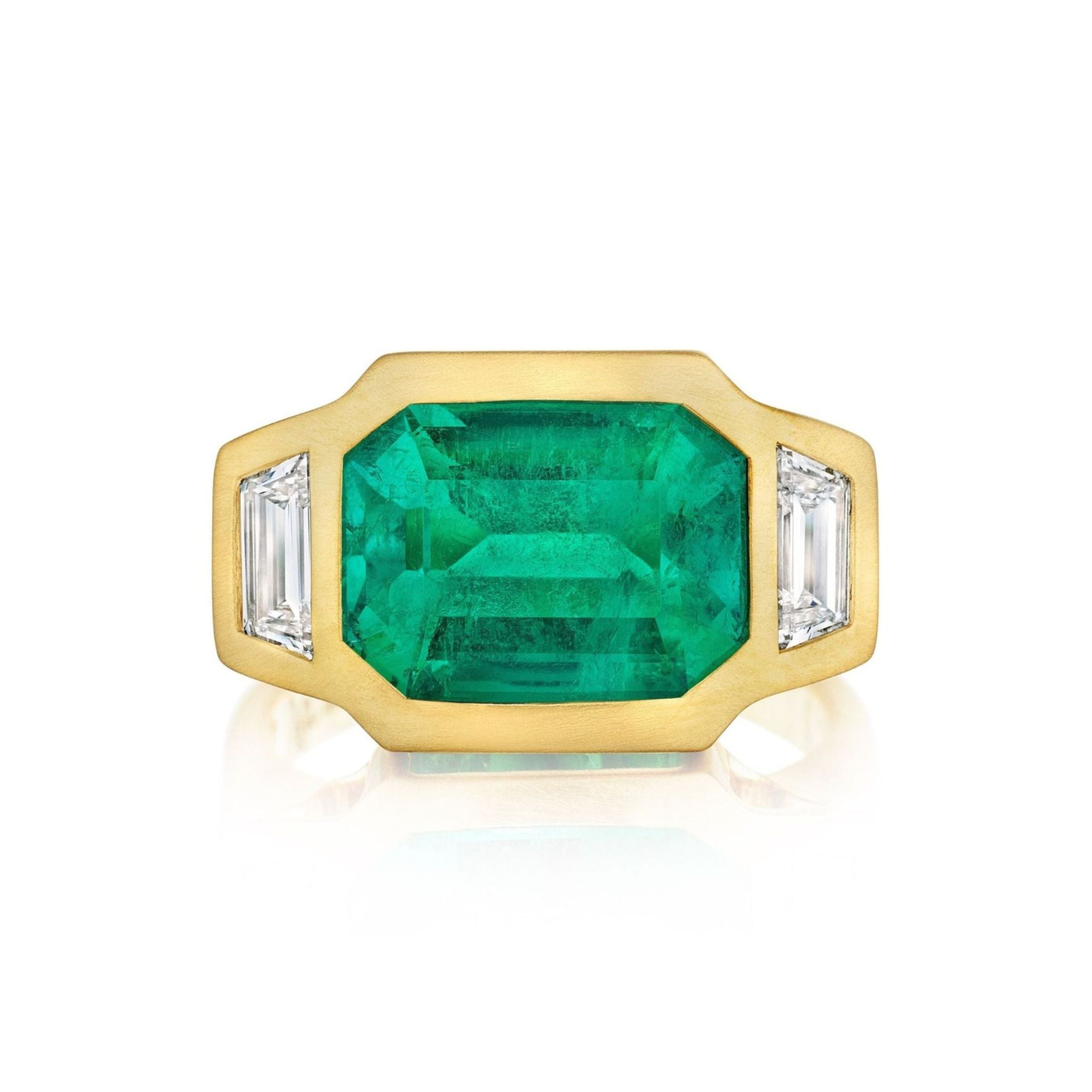 Introducing the Bezel Set East-West Emerald Cut Emerald Three Stone Ring with Trapezoid Diamond Side Stones in Matte Yellow Gold, showcasing a bold rectangular emerald-cut emerald set horizontally at the center, bezel-set in rich matte 18k yellow gold and accented by sparkling trapezoid diamond side stones on either side.