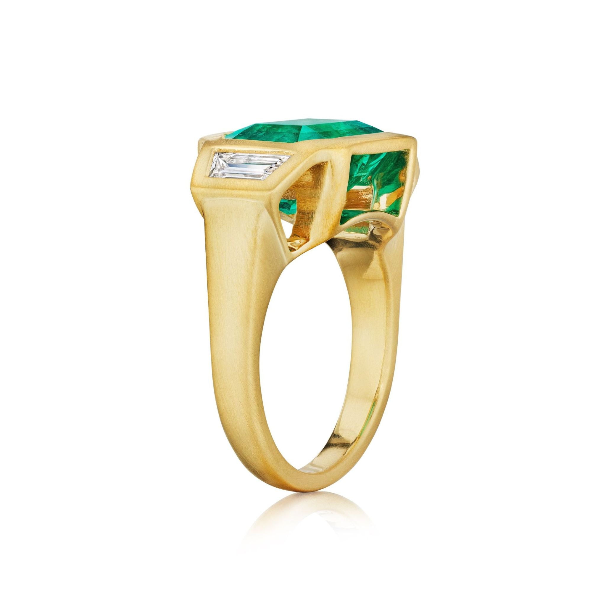Bezel Set East-West Emerald Cut Emerald Three Stone Ring with Trapezoid Diamond Side Stones in Matte Yellow Gold, featuring a vibrant green emerald center stone and sparkling trapezoid diamond accents, elegantly displayed on a white background.