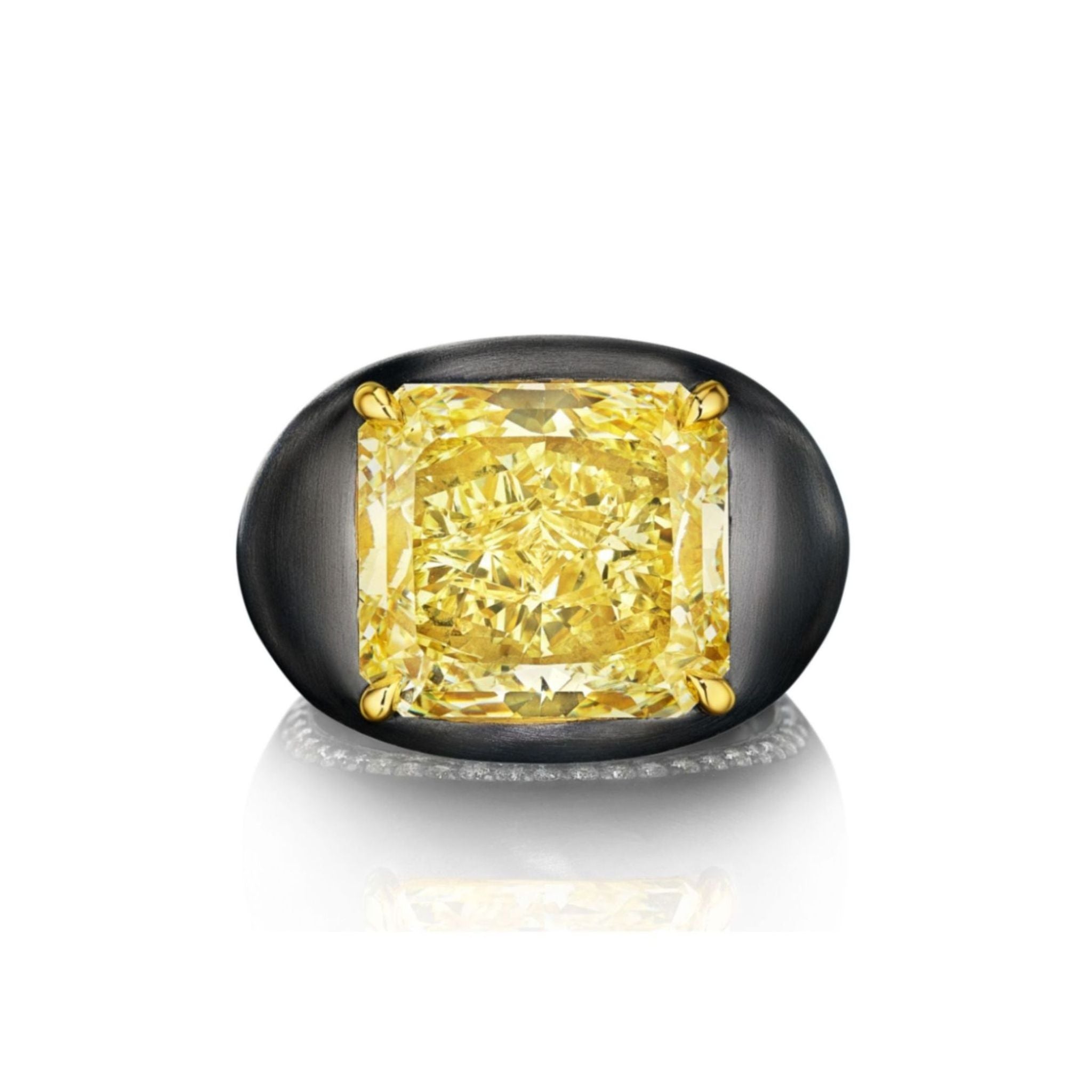 The East-West Prong Set Radiant Cut Yellow Diamond Signet Ring in Black Rhodium features a large radiant cut yellow diamond secured by four gold prongs atop an oval black rhodium platinum band, displayed above a reflective surface.