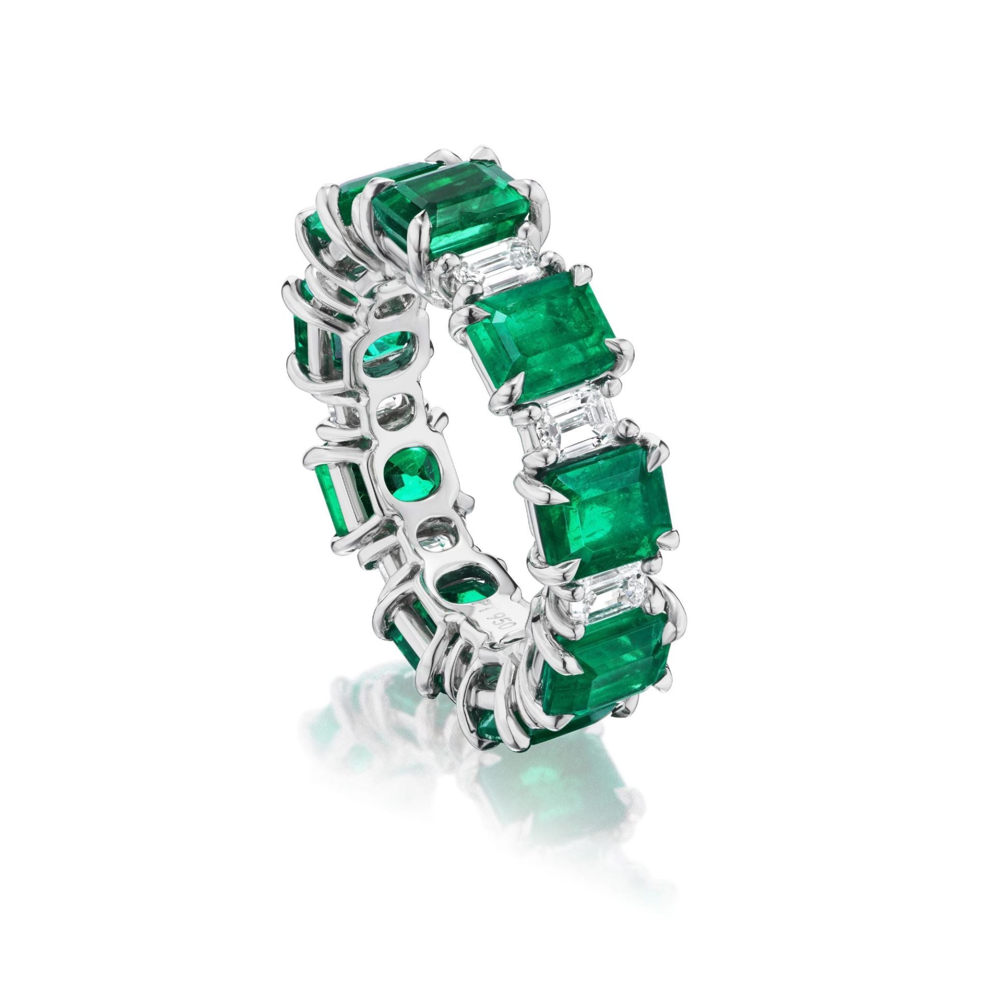 An eternity band named the Alternating Emerald Cut Diamond and Emerald Eternity Band, crafted in platinum, displays a seamless row of rectangular emerald gemstones set in prongs with smaller clear diamonds alternating between each emerald. Reminiscent of classic emerald cut designs set in 18k white gold, the ring is shown upright against a white background.