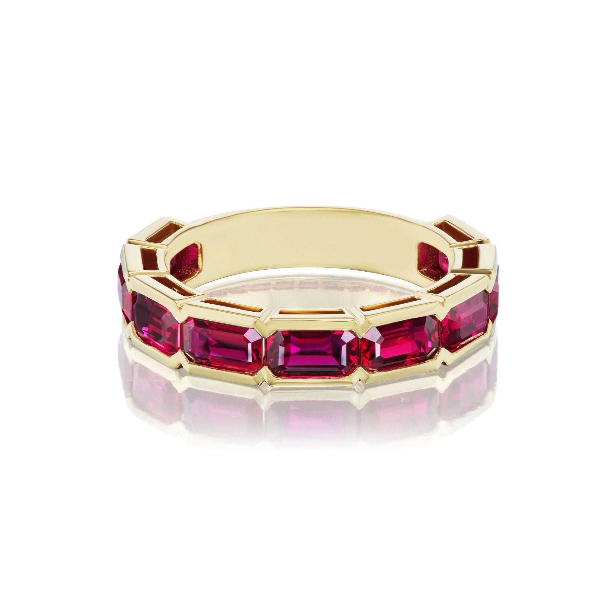 A dazzling Bezel Set East-West Emerald Cut Ruby Half-Eternity Band in 18k yellow gold, featuring emerald-cut rubies arranged in an east-west bezel setting along the band, displayed on a reflective white surface.