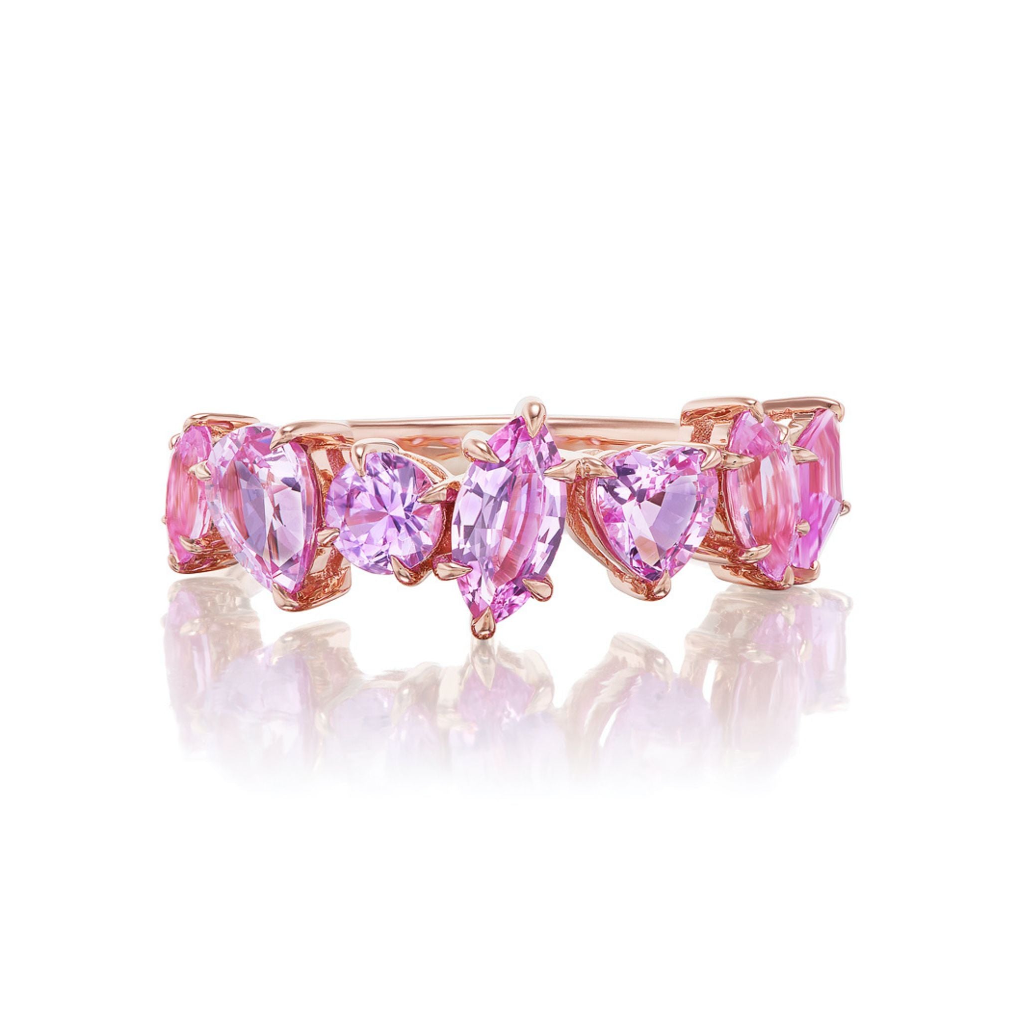 The Sapphire Mixed Shape Cluster Ring, crafted in rose gold, features a continuous row of pink and purple gemstones—including heart-shaped and oval sapphires—arranged in an eternity band design. The ring is displayed on a white reflective surface.