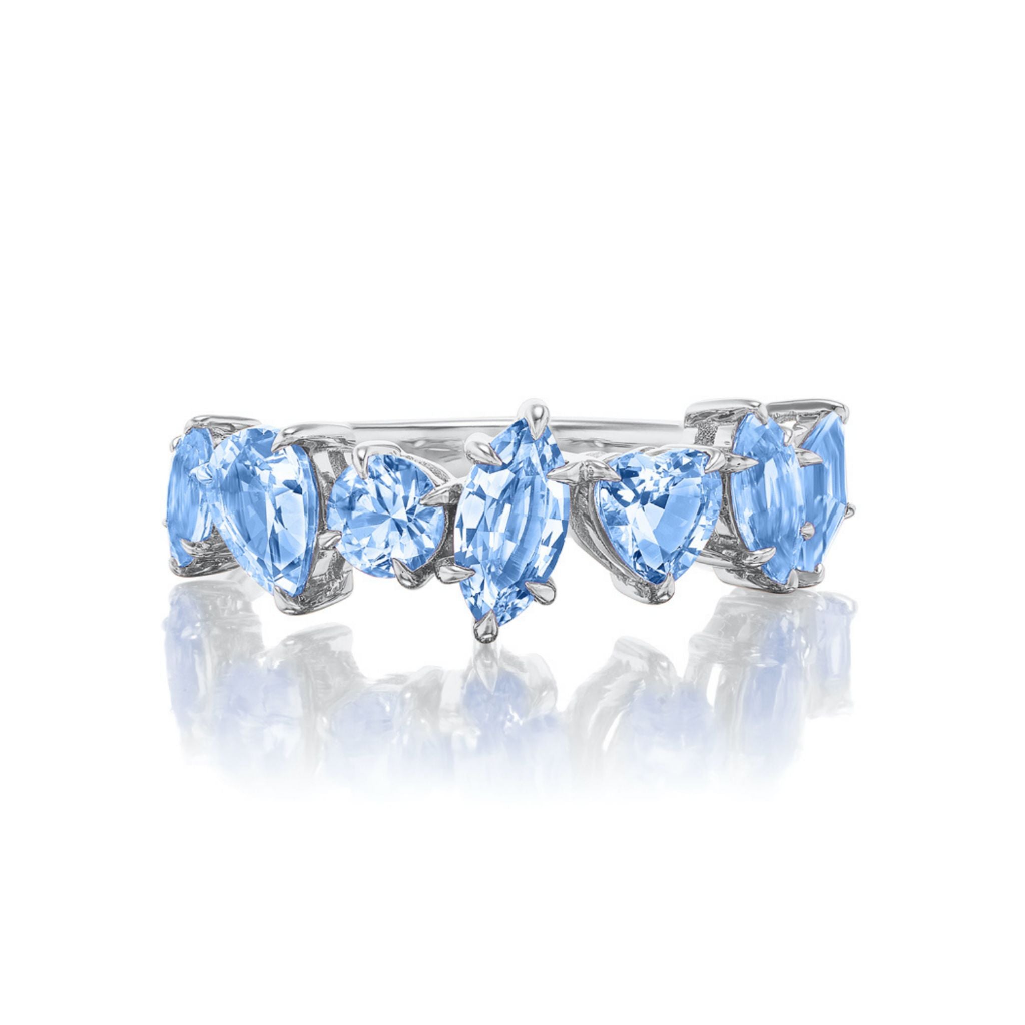 The Sapphire Mixed Shape Cluster Ring is a silver half eternity band showcasing five light blue sapphires in marquise, round, and heart cuts, arranged in a row. It is elegantly displayed on a white reflective surface.