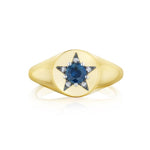 The America250 Star Signet Ring in Yellow Gold and Platinum is handcrafted in New York City from 18k yellow gold, featuring a round blue gemstone at the center of a star-shaped arrangement of small clear stones on a flat, oval face.