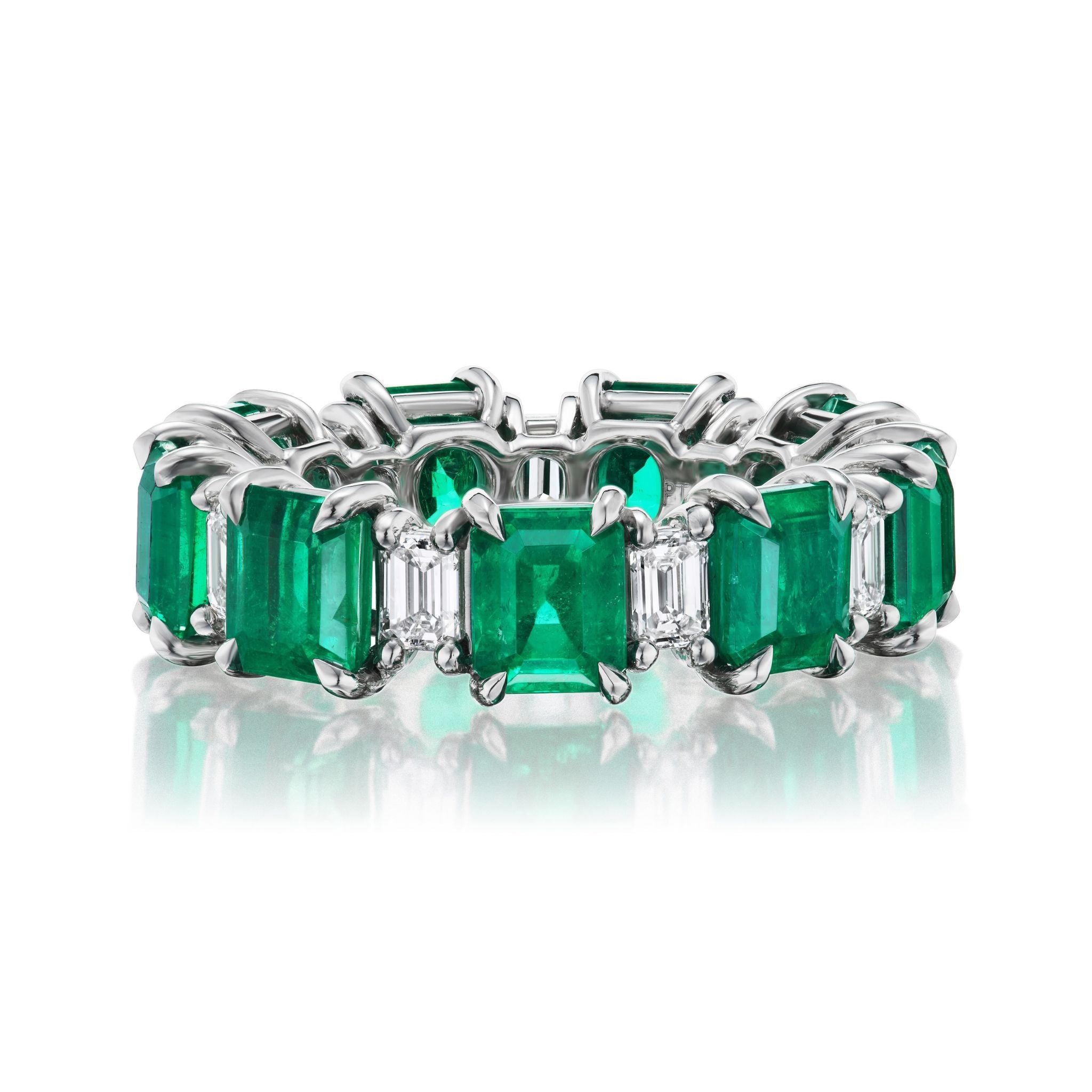 The Alternating Emerald Cut Diamond and Emerald Eternity Band features a platinum band with rectangular emeralds and diamonds set in prongs, creating an elegant and luxurious continuous design.