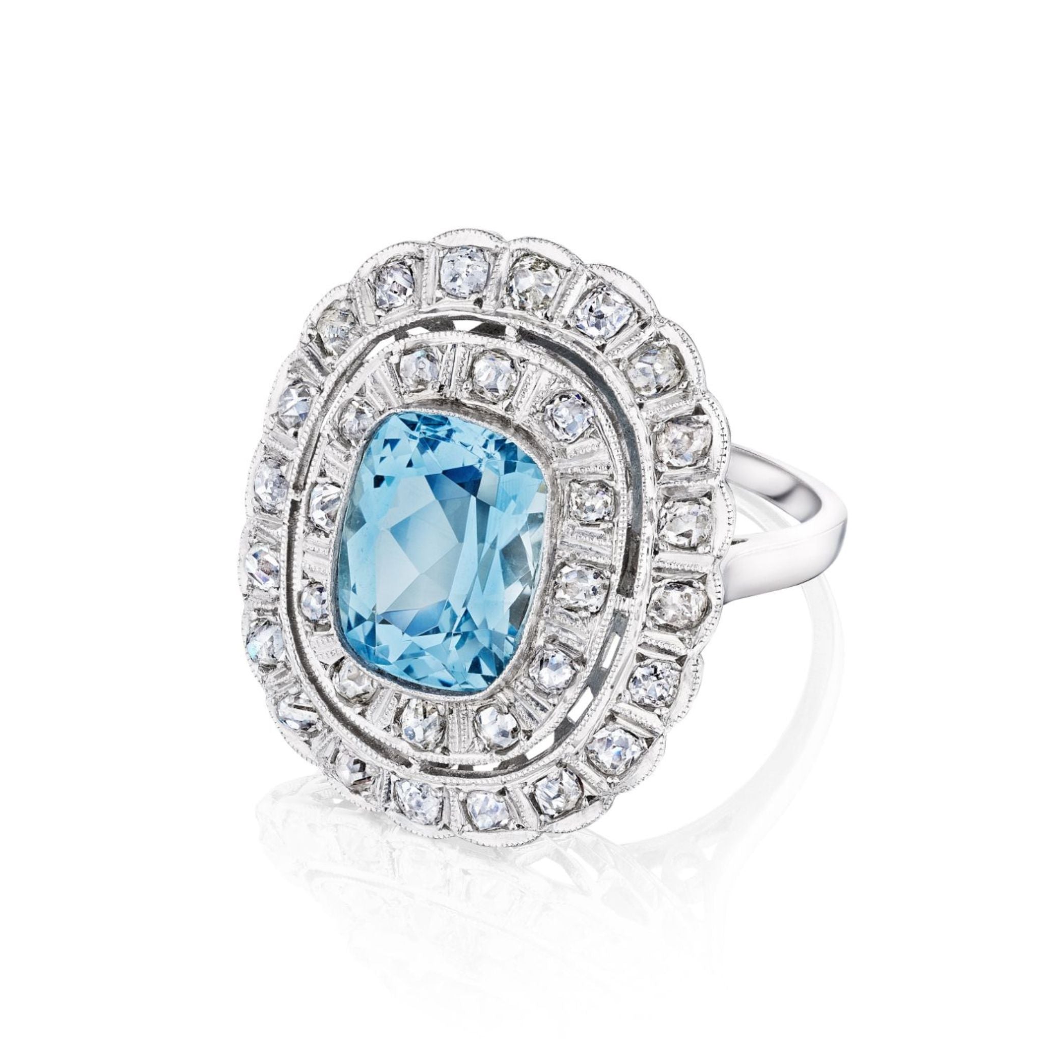 The Aquamarine and Diamond Ring features a large rectangular cushion-cut aquamarine at the center, framed by two rows of round diamonds, set in platinum and displayed on a white background.
