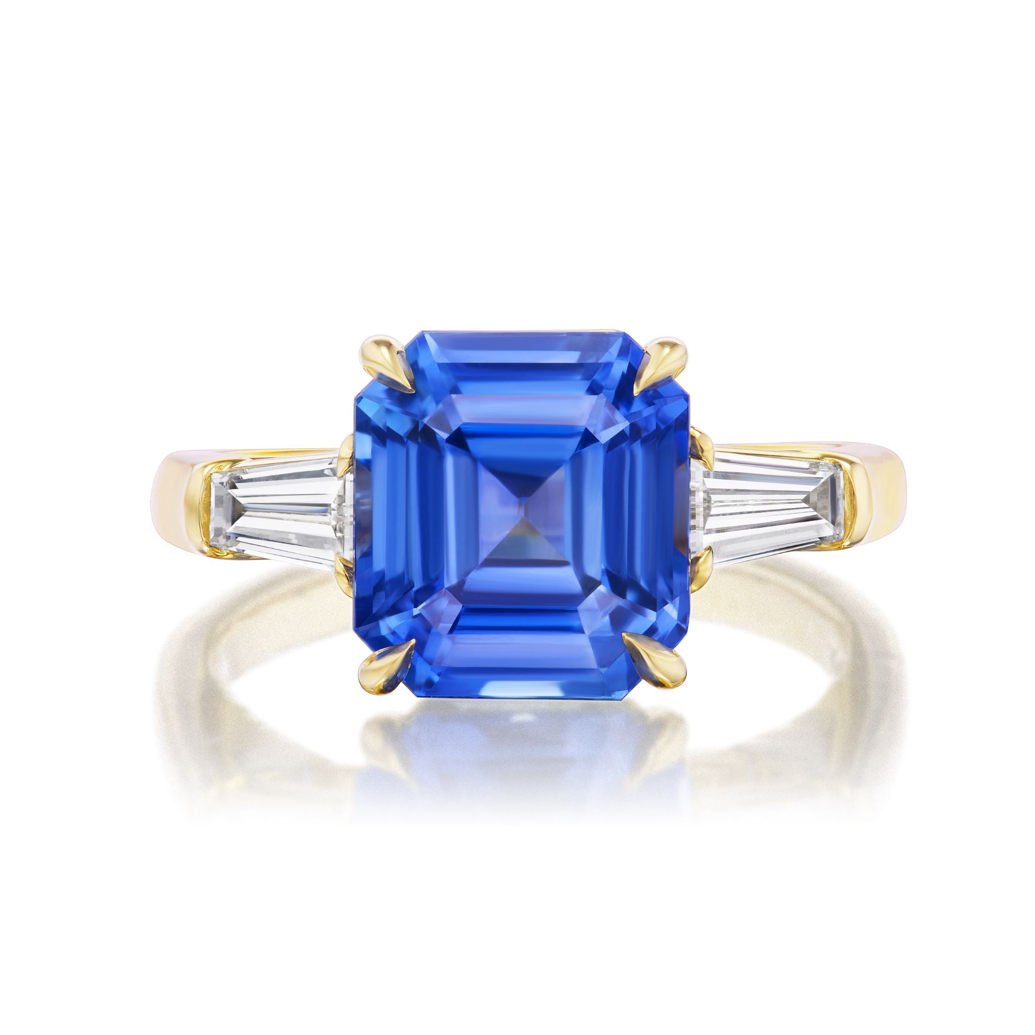 The Asscher Cut Sapphire Engagement Ring features a central sapphire and tapered baguette diamond side stones, all set in 18K yellow gold.