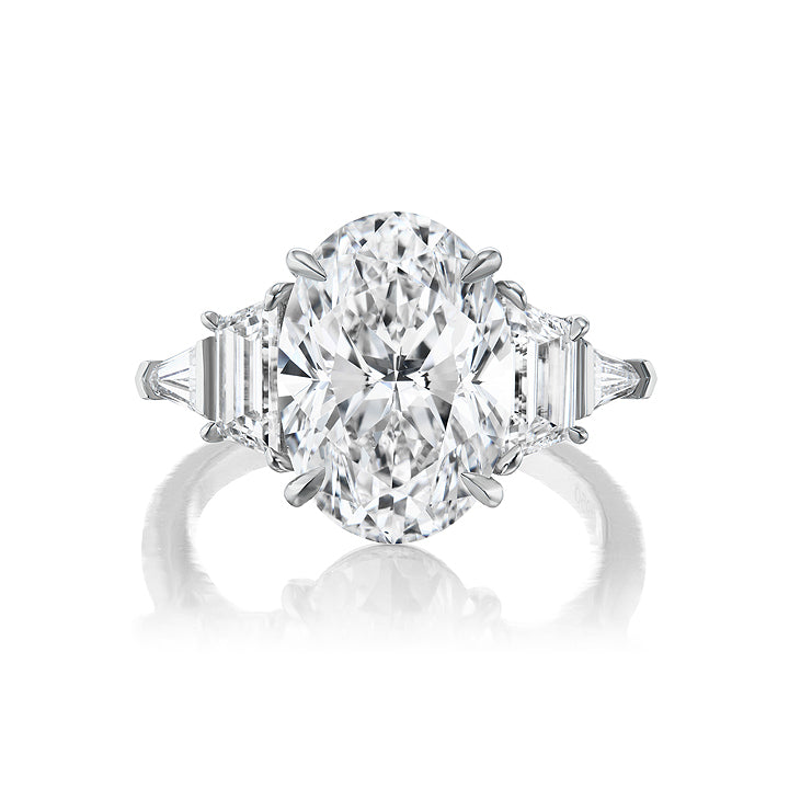The Oval Diamond Engagement Ring features trapezoid and tapered baguette side stones set on a white metal band, shown against a white background.