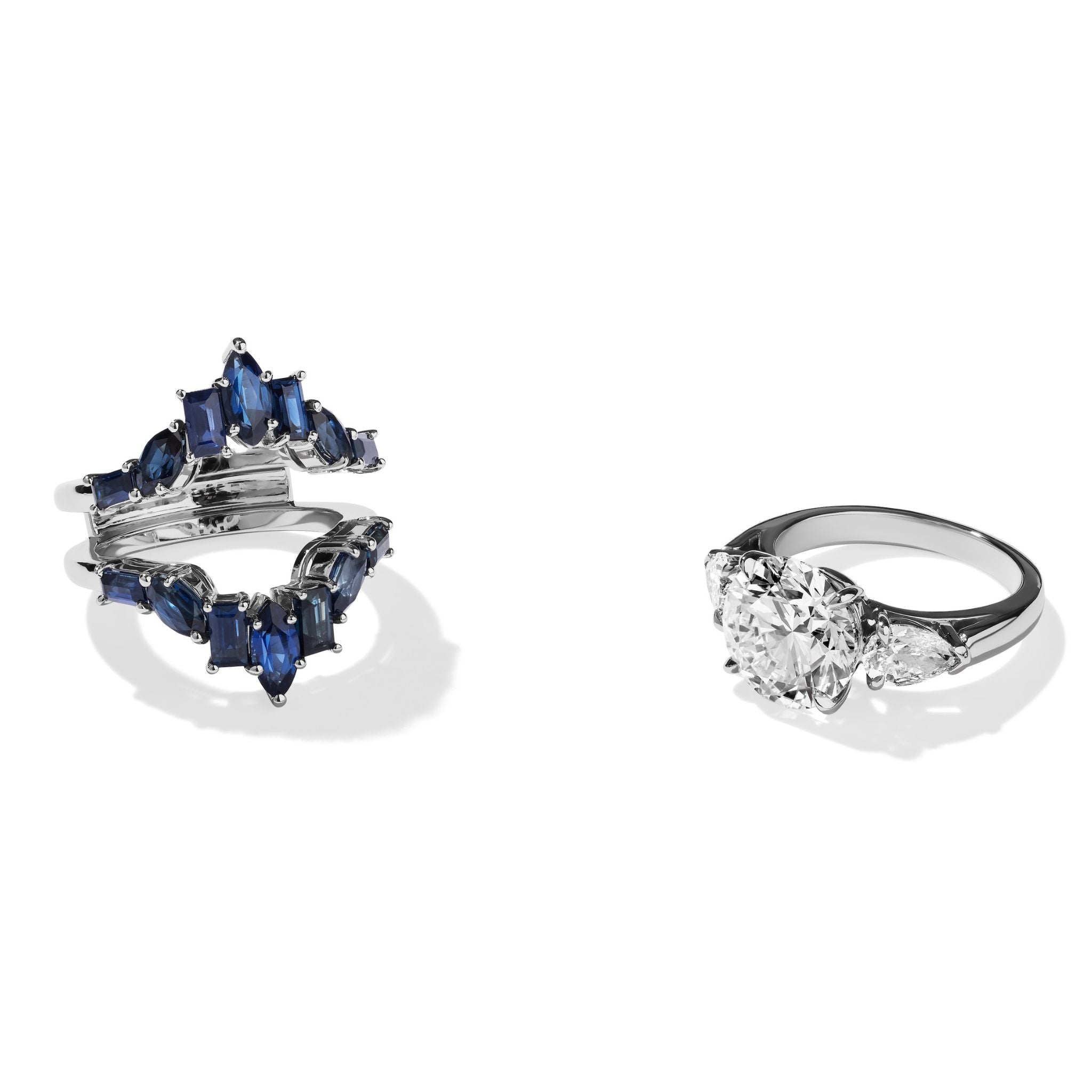 Two rings are shown on a white background: one is a Baguette and Marquise Sapphire Engagement Ring Jacket in White Gold with a unique split-band design; the other is a classic white gold engagement ring with three clear gemstones.
