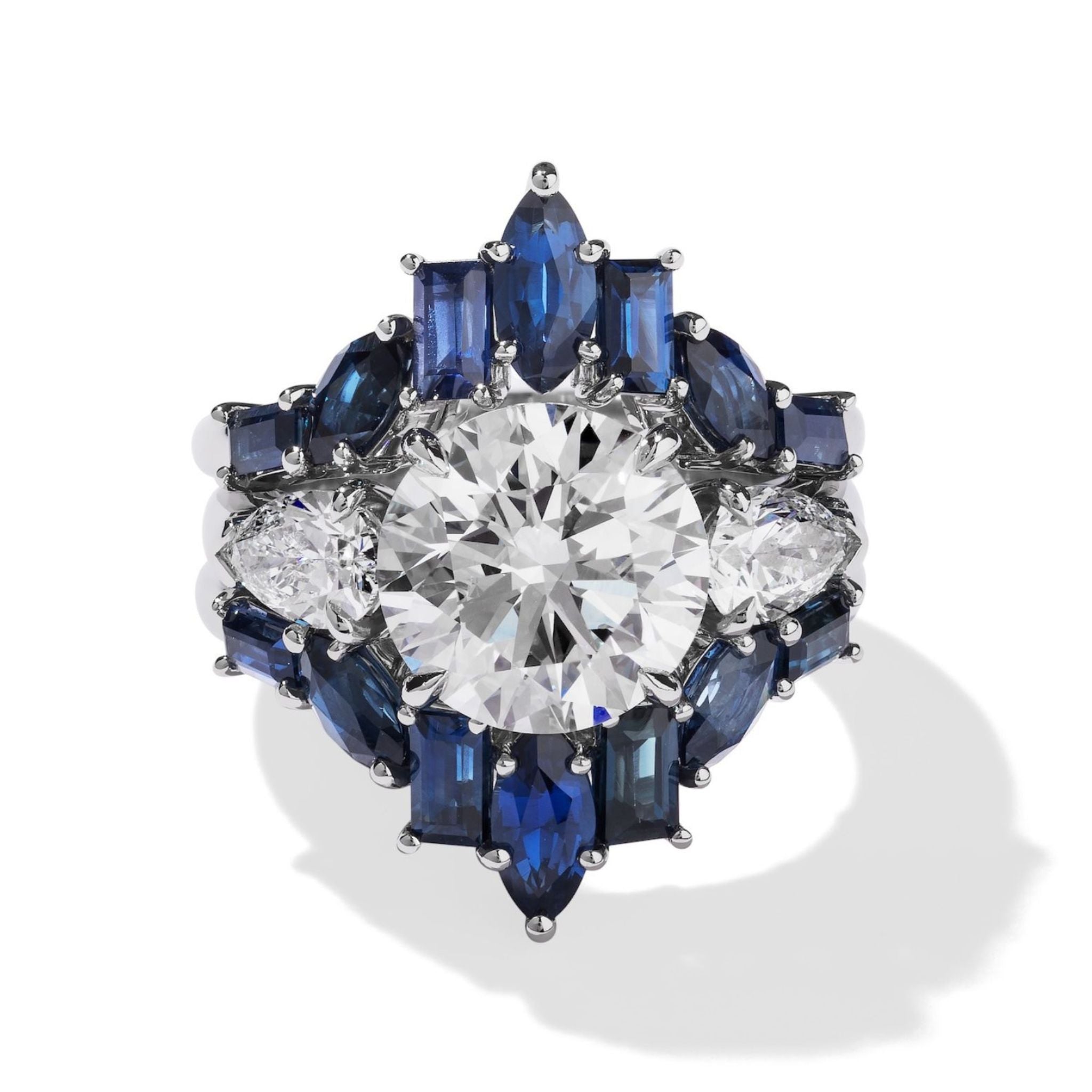 A silver ring with a round diamond, accented by pear-shaped diamonds and blue baguette sapphires in a floral design—perfect when paired with the Baguette and Marquise Sapphire Engagement Ring Jacket in White Gold.