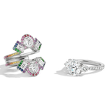 A Cross Motif Ring Jacket in white gold features round and emerald cut diamonds with a rainbow sapphire pavé halo and band, displayed on a white background.