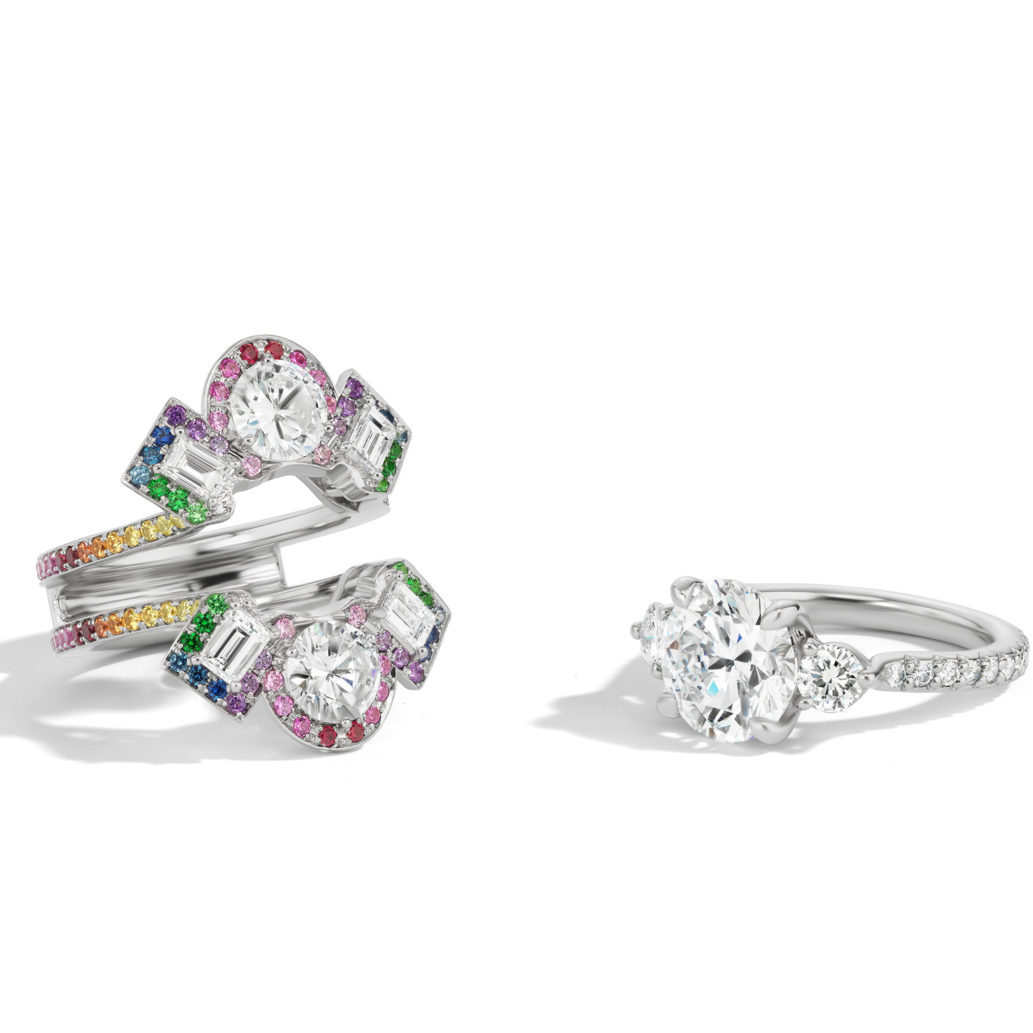 A Cross Motif Ring Jacket in white gold features round and emerald cut diamonds with a rainbow sapphire pavé halo and band, displayed on a white background.