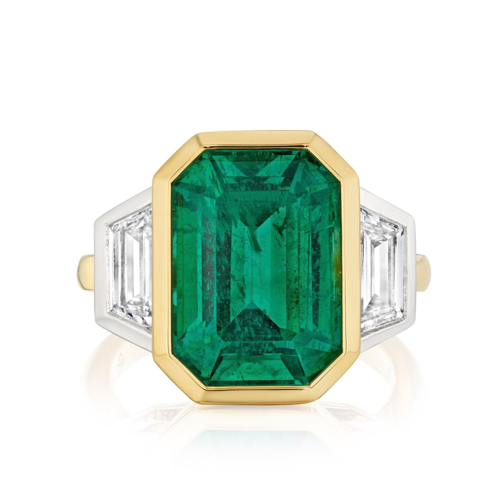 The Bezel Set Emerald Cut Emerald Engagement Ring in yellow gold and platinum features a large emerald center with trapezoid baguette diamond side stones on a sleek band.