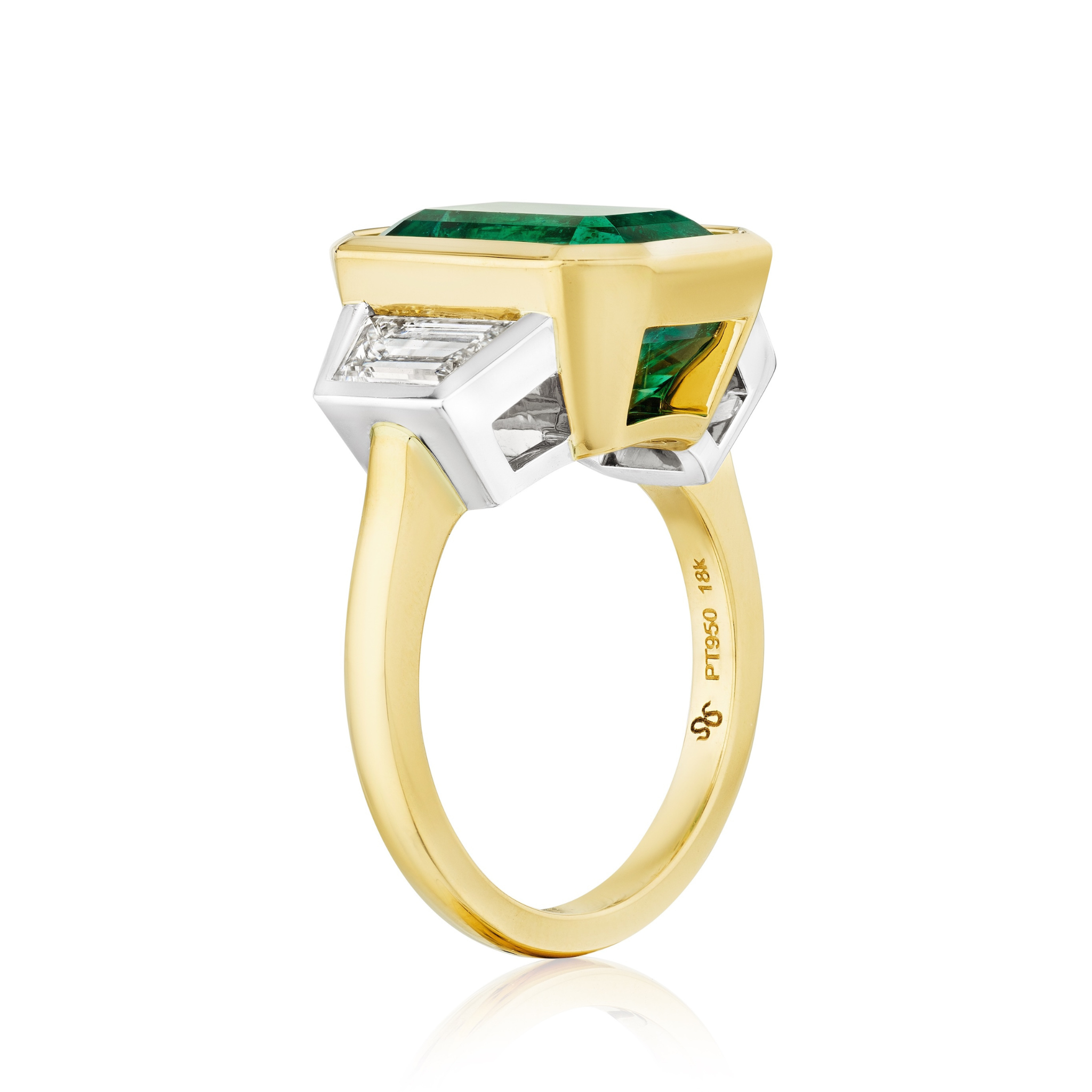 The Bezel Set Emerald Cut Emerald Engagement Ring in yellow gold and platinum features a center emerald, trapezoid baguette diamond side stones, and an engraved 18K yellow gold band.