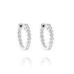 The Bezel Set Hexagon Huggies with Round Brilliant Diamonds showcase sparkling bezel-set round diamonds along the front of each silver-finished hexagonal hoop, displayed on a white background with a soft reflection.