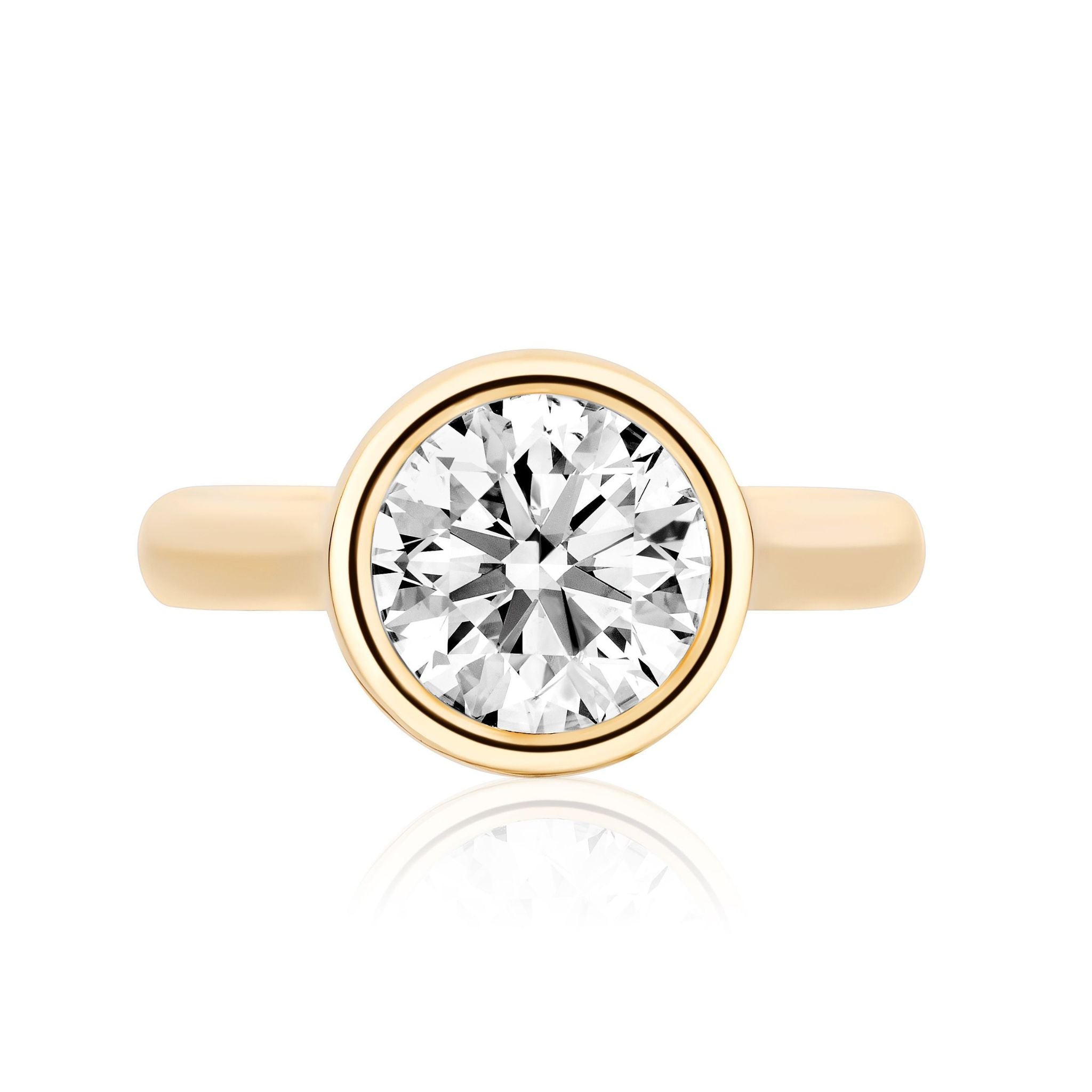 The Bezel Set Round Diamond Engagement Ring features a round diamond in a bezel setting, displayed against a white background with a subtle reflection below.