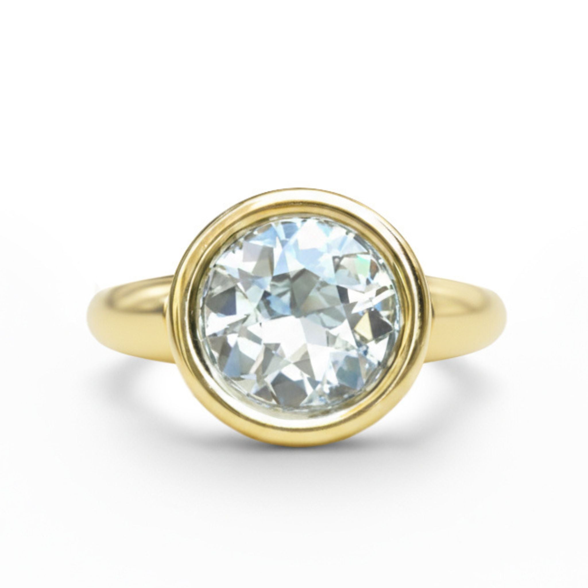 The Bezel Set Round Diamond Engagement Ring in Yellow Gold features a round, clear diamond in a bezel setting, shown against a white background.