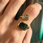 A hand wearing the Bezel Set Toi et Moi Wrap Ring in yellow gold, featuring a round diamond and an emerald cut green tourmaline.
