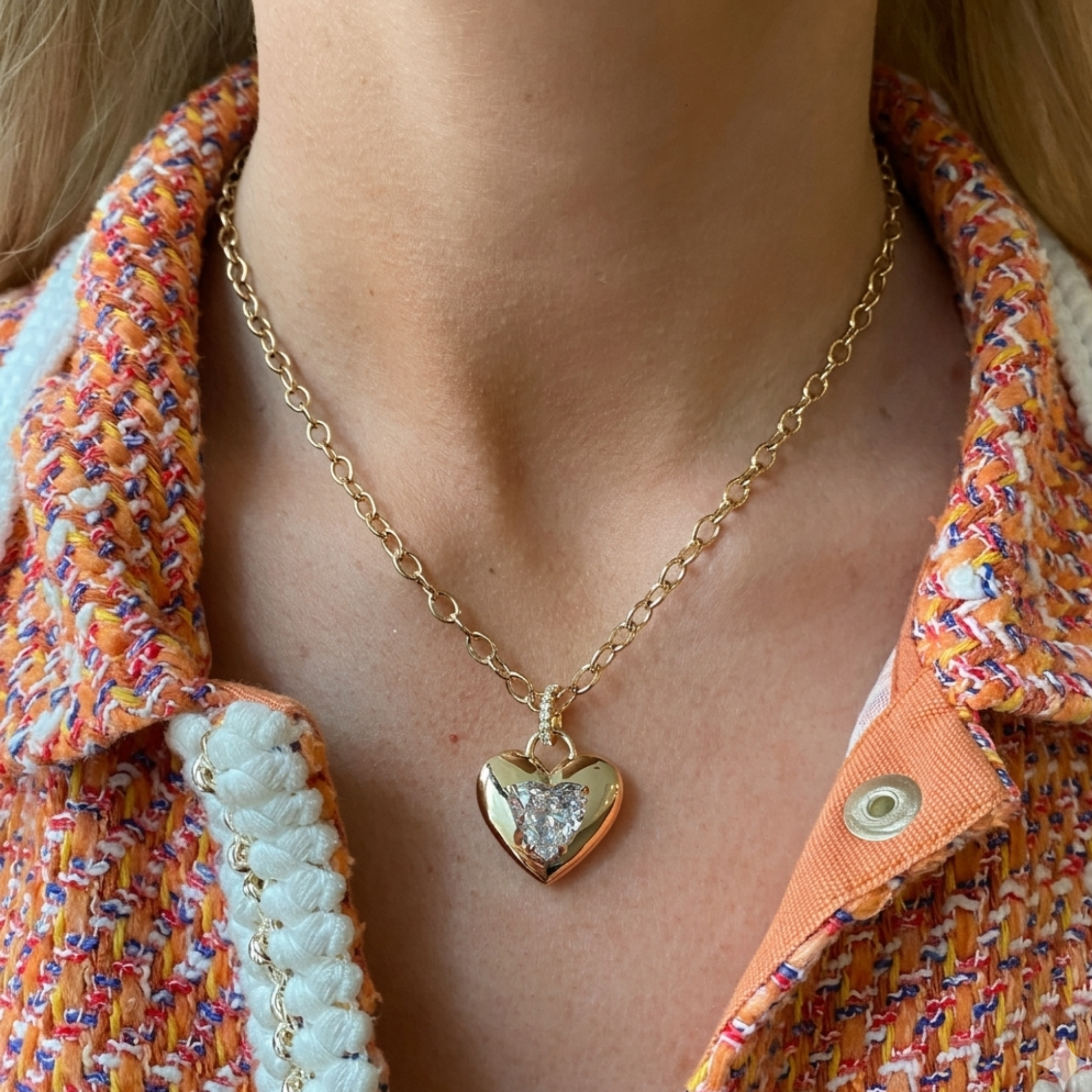 A close-up of a woman wearing the Burnish Set Heart Shape Diamond Pendant, featuring a gold heart design with a central diamond, styled with a textured multicolored orange and white jacket.