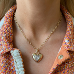 Close-up of a person wearing the Burnish Set Heart Shape Diamond Pendant—a gold chain necklace with a diamond center—paired with a textured orange and white jacket featuring a visible button.