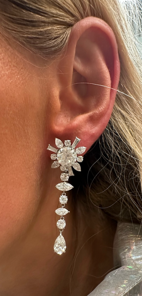 A close-up of a woman's ear showcases the Bespoke Mixed Shape Diamond Ear Jacket in White Gold, featuring floral and drop designs. The sparkling luxury piece stands out against her light skin and blonde hair.