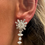 A close-up of a woman wearing the Mixed Shape Diamond Ear Jacket in White Gold, featuring sparkling, floral-shaped diamonds in a dangling design. Her skin and light brown hair are partially visible.