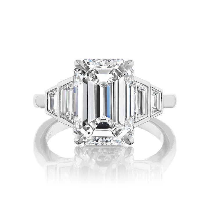 The Echo Emerald Cut Diamond Engagement Ring features a bezel-set emerald-cut center diamond with graduating trapezoid side stones, showcased against a white background.
