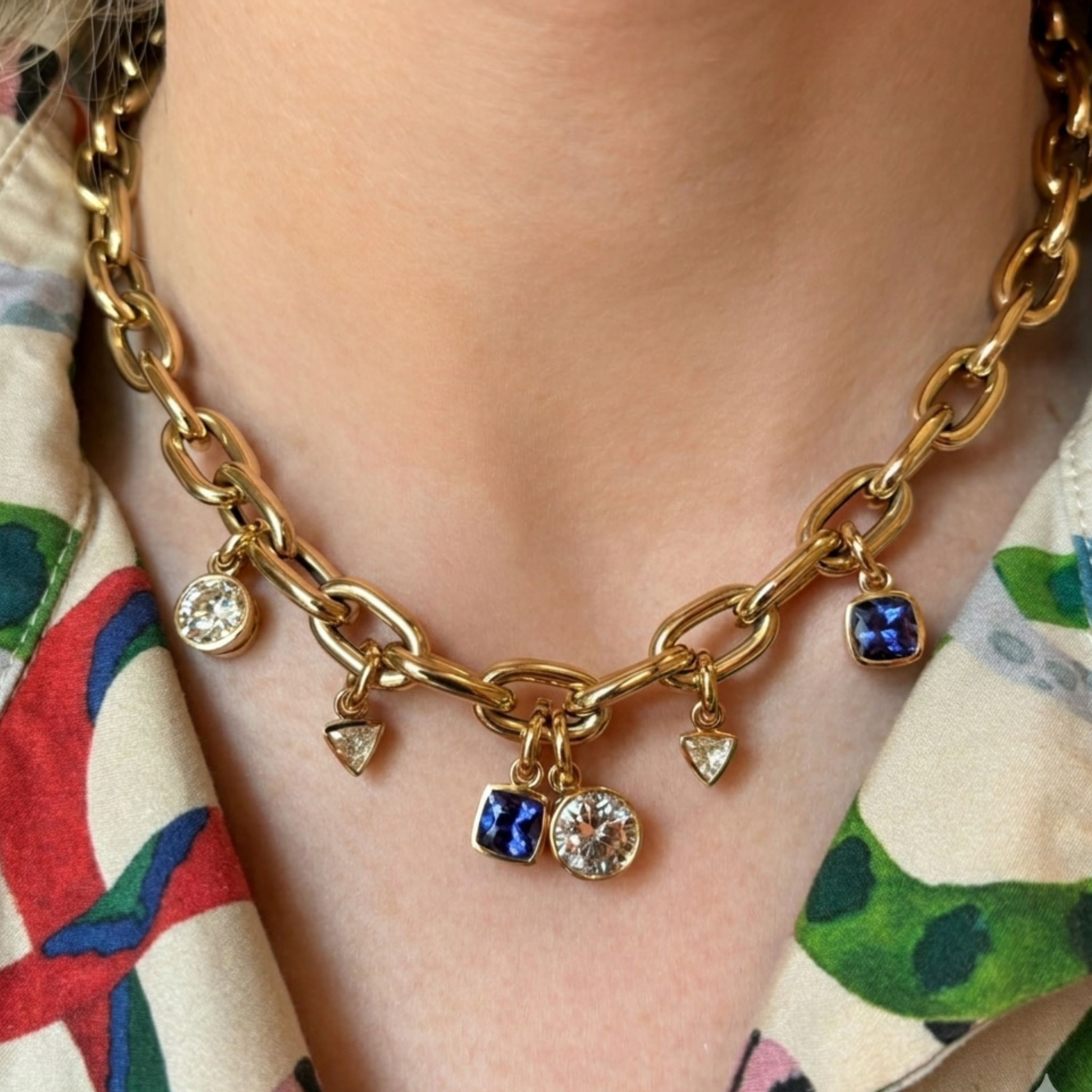 A close-up of the Chain Necklace in Yellow Gold featuring bezel set sapphires, diamonds, and emeralds in mixed shapes, worn over a colorful patterned shirt.
