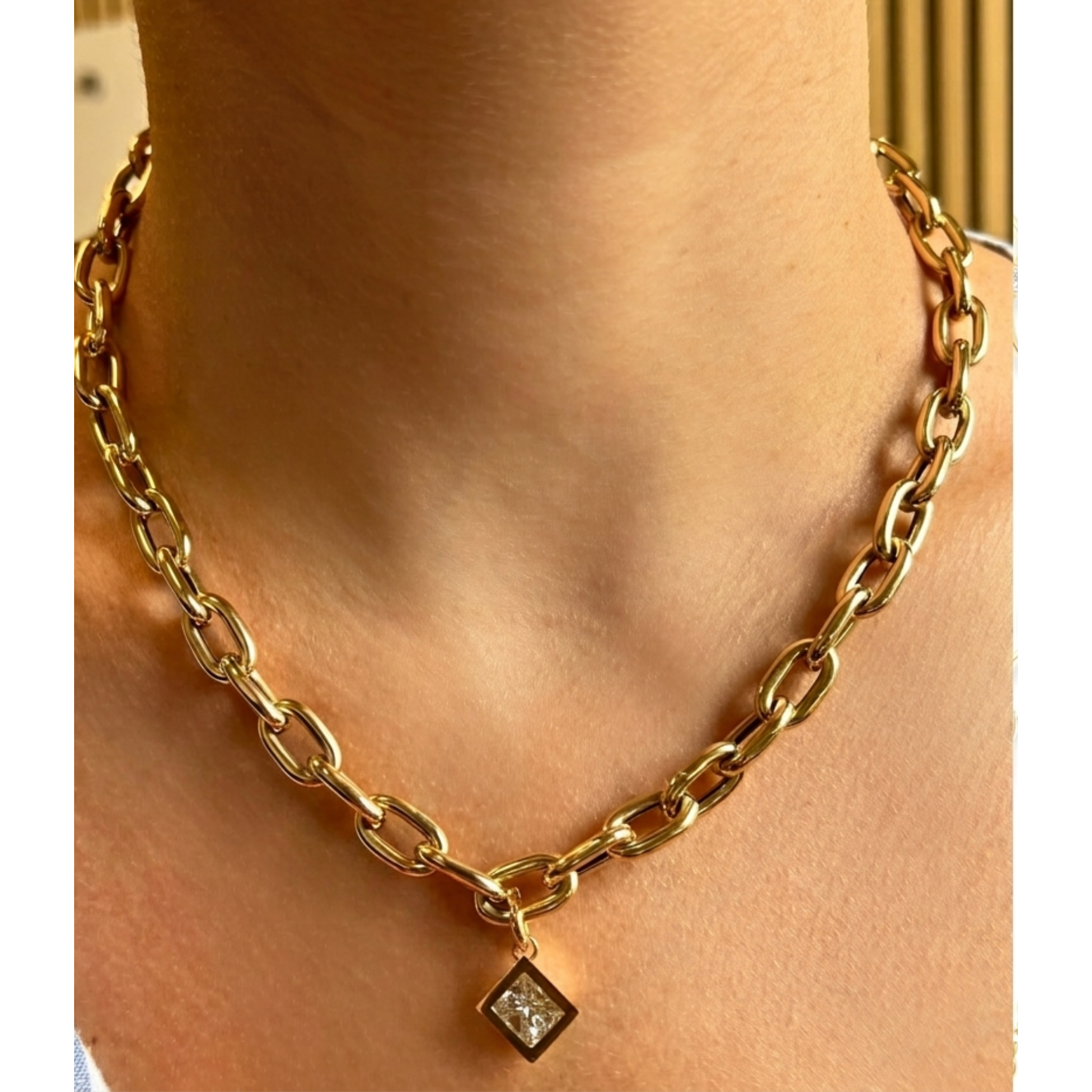 A Chain Necklace with Diagonal Bezel Set Elongated Square Diamond Charm in Yellow Gold, featuring thick links and an 18K yellow gold pendant with a clear elongated square diamond, worn around the neck.