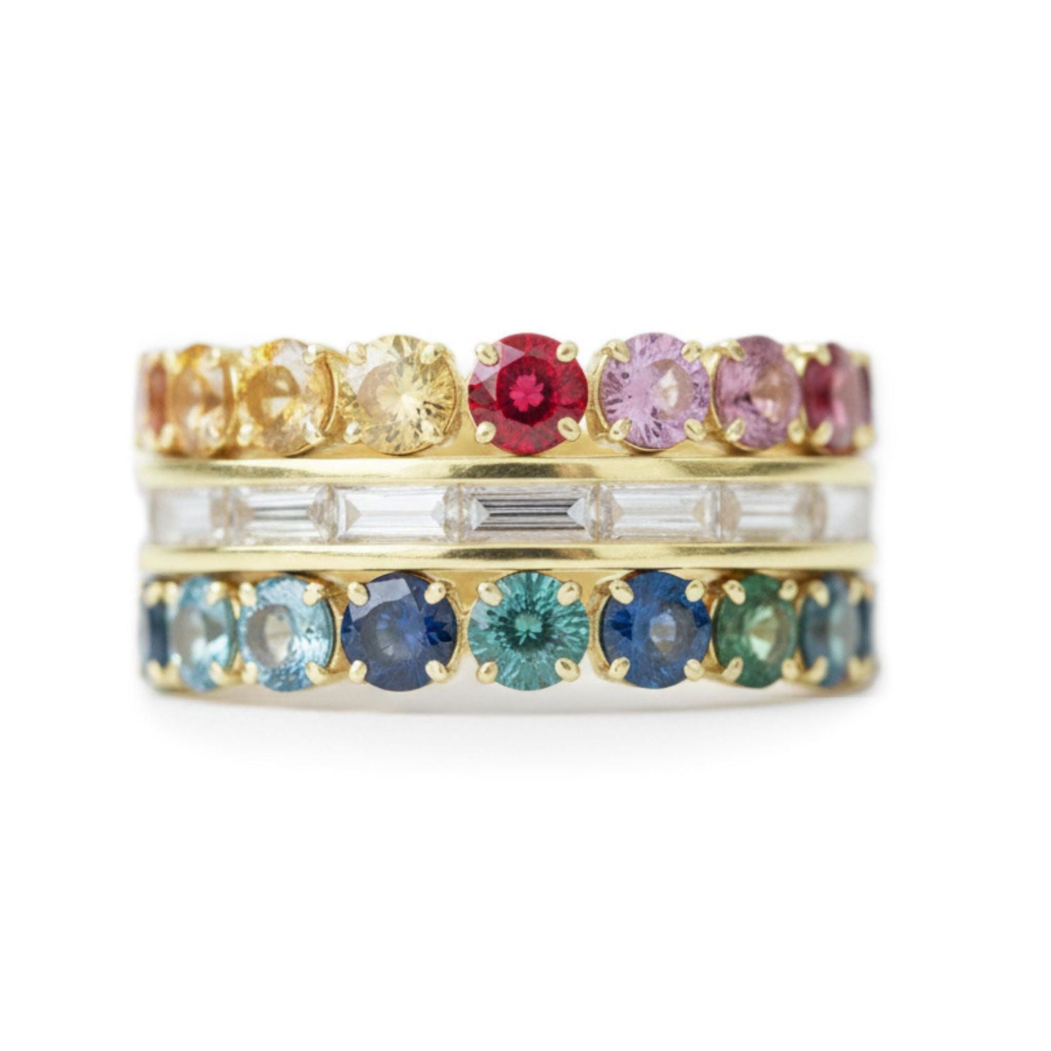 A yellow gold ring features channel-set baguette diamonds flanked by multicolor round sapphires in vibrant hues, creating a striking stacked look.