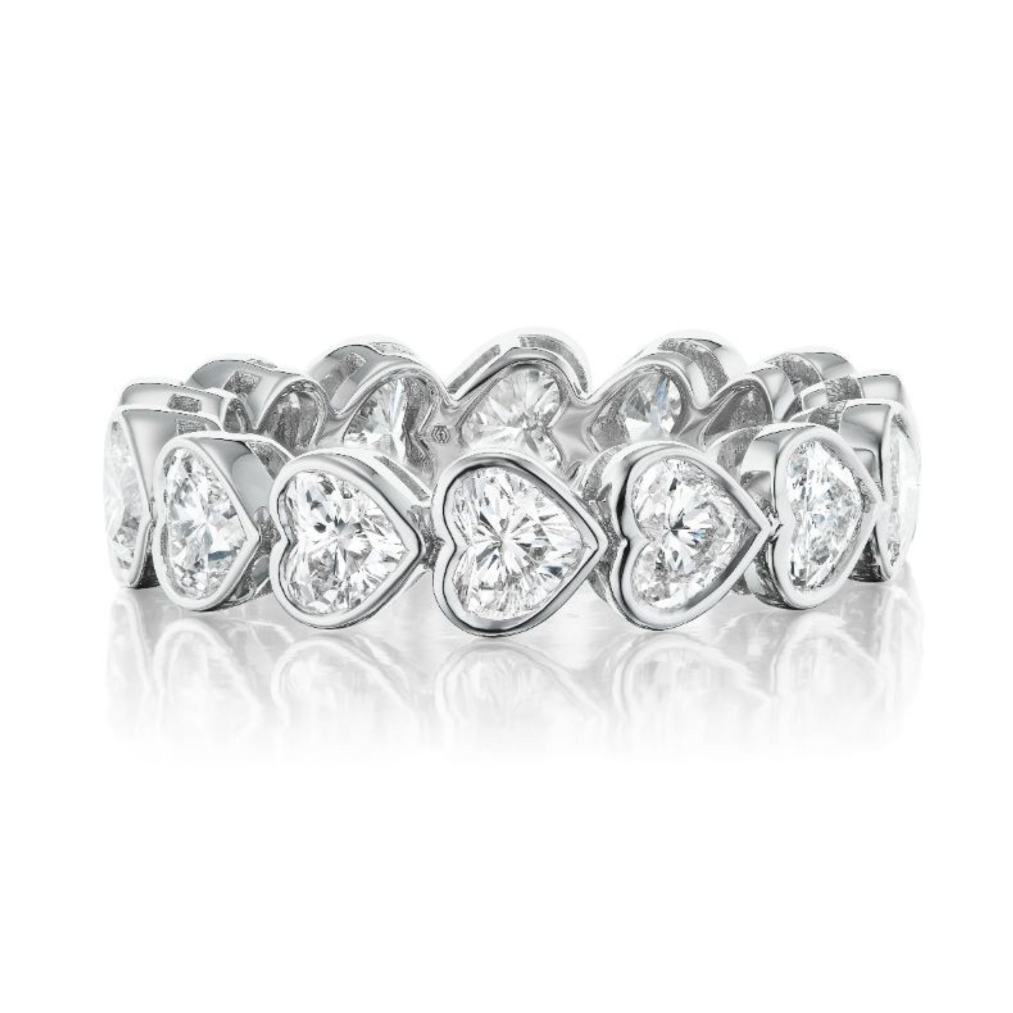 The Chasing Hearts Bezel Set Eternity Band showcases heart-shaped diamonds in a continuous row, sparkling in 18K white gold, displayed on a white reflective surface.