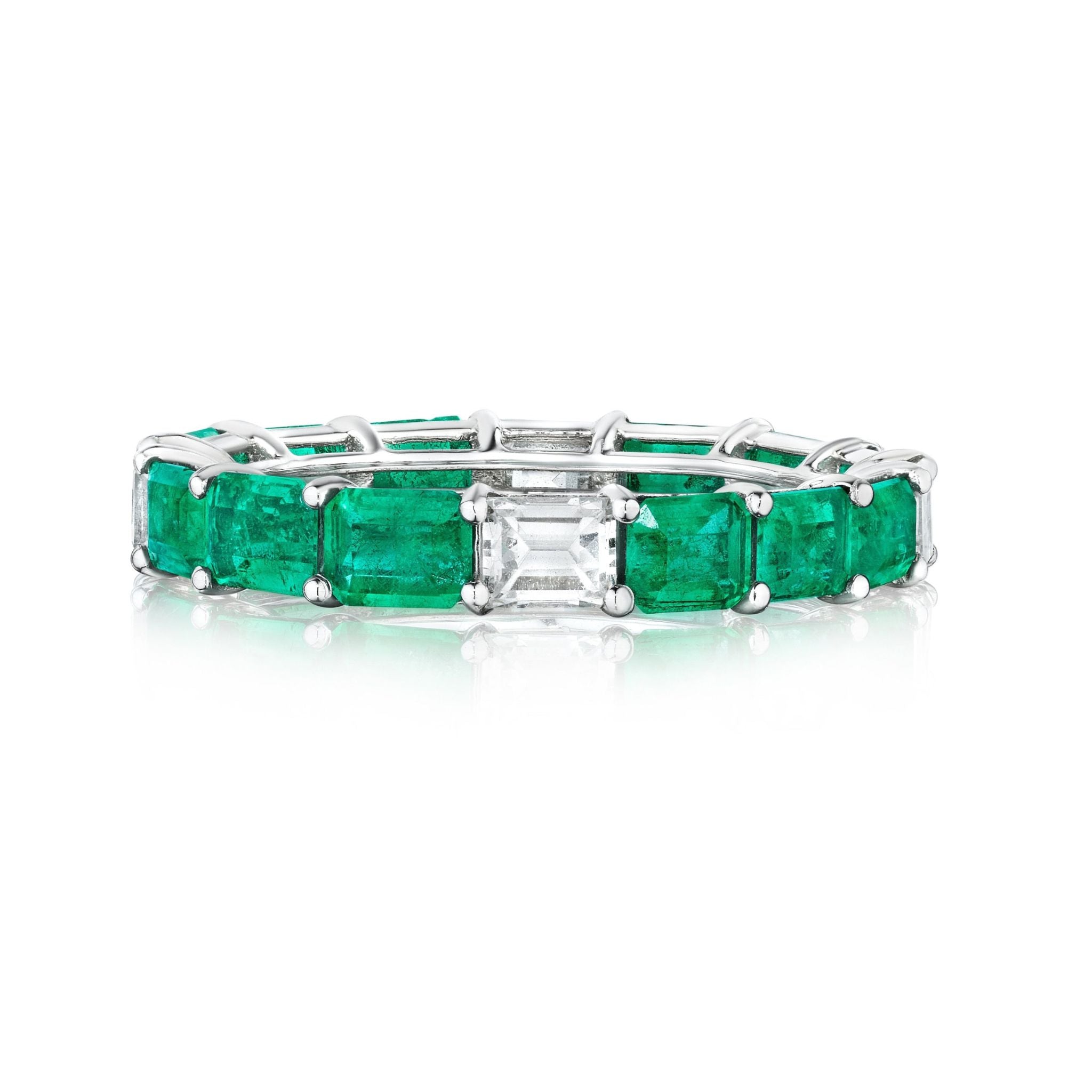 The East-West Emerald Cut Emerald and Diamond Eternity Band in White Gold showcases alternating emerald-cut emeralds and a center emerald-cut white diamond in an elegant prong setting.